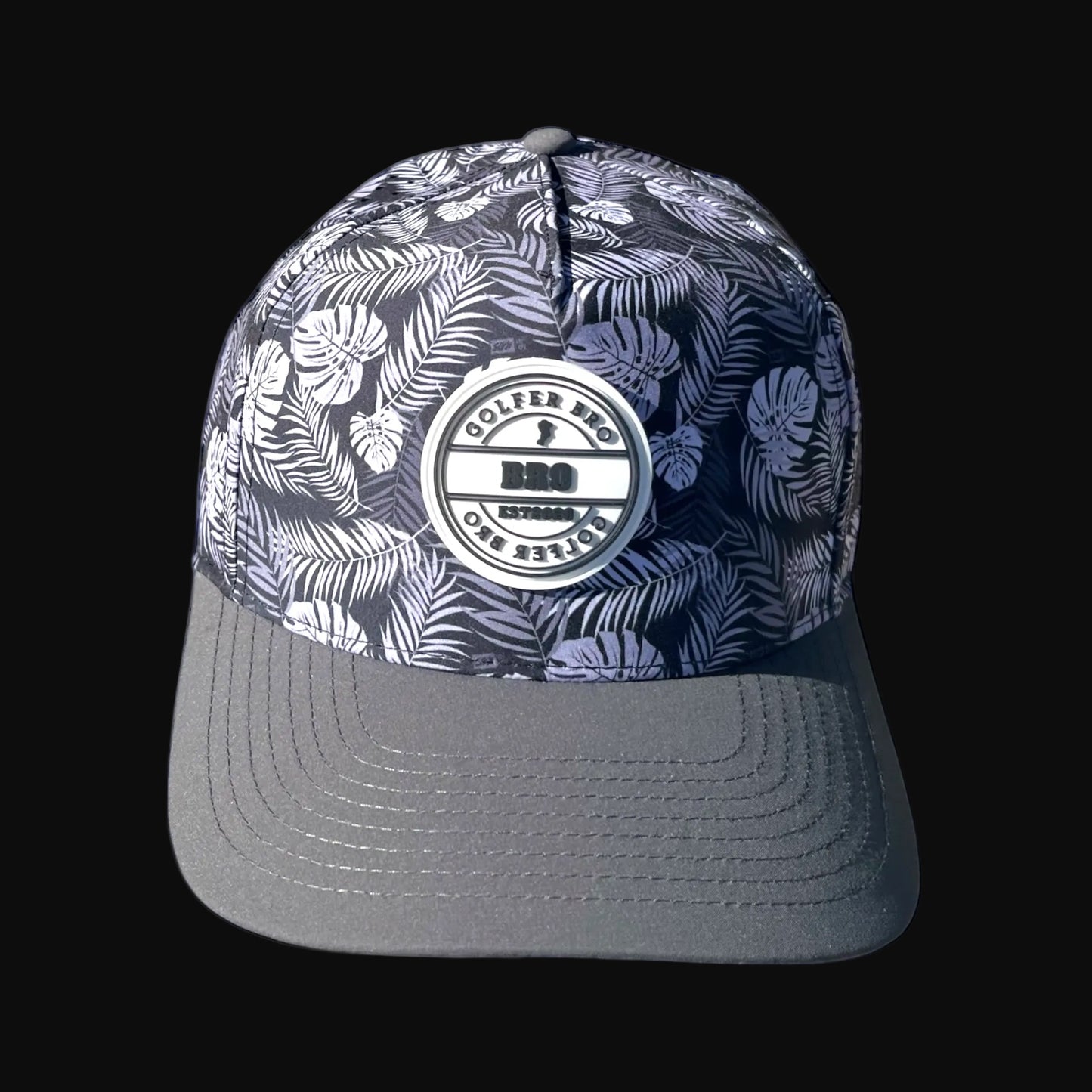 Golfer Bro perforated performance cap with a tropical leaf print and grey bill. Features a moisture-wicking sweatband and snapback closure.
